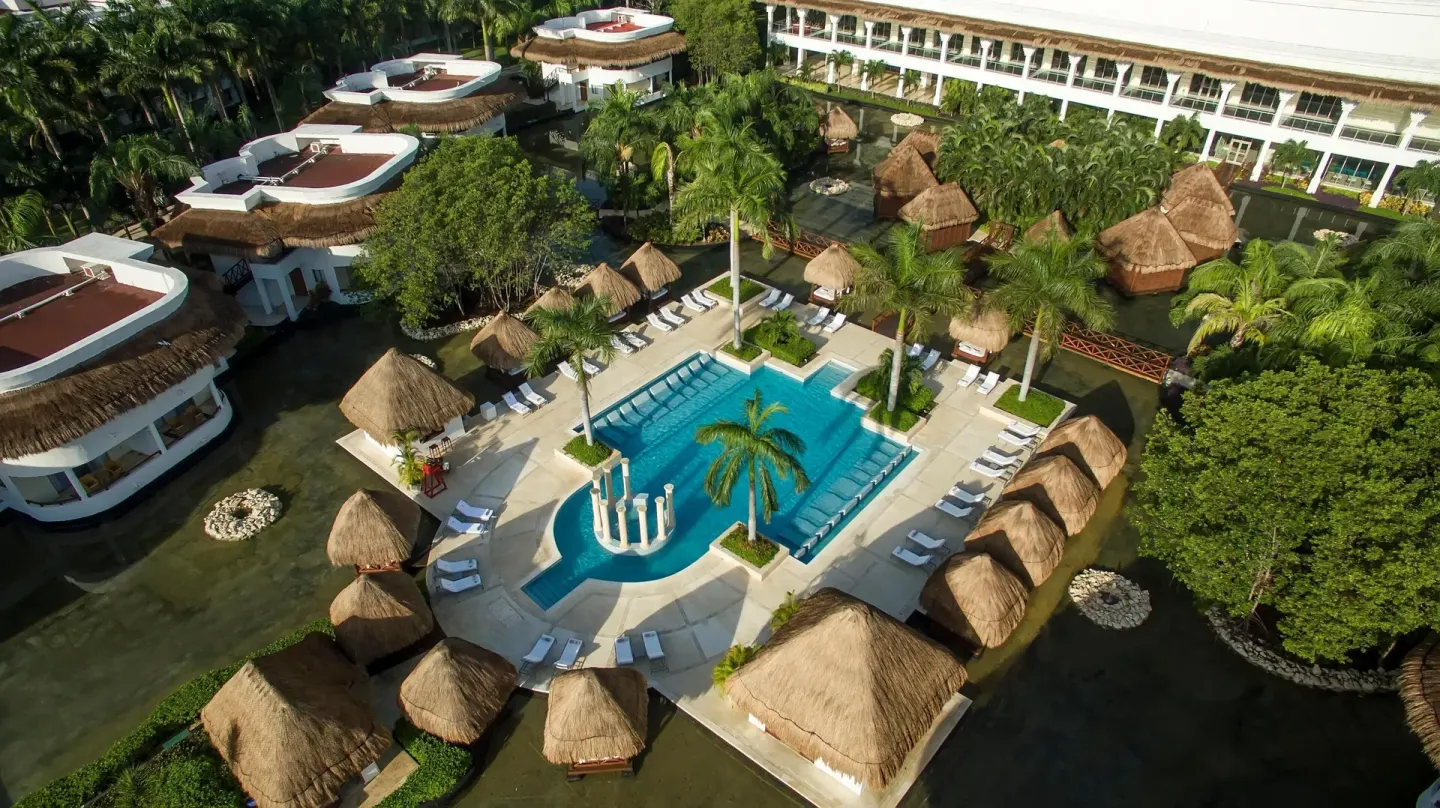 Aerial view of a pool courtyard with palapas and guest buildings at Grand Sunset Princess.