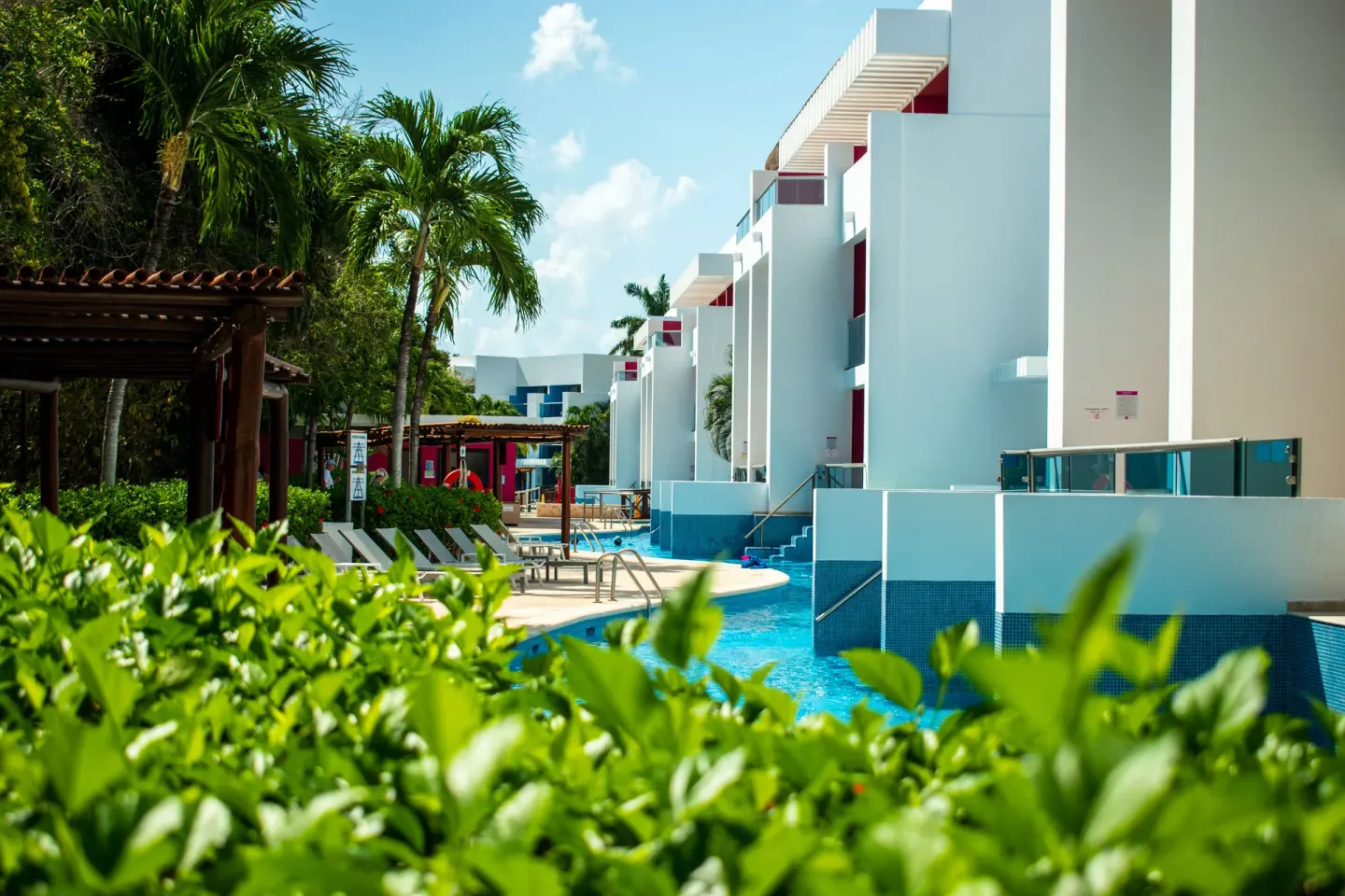 Pool area with hedges, palms, loungers and white buildings at Grand Sunset Princess.