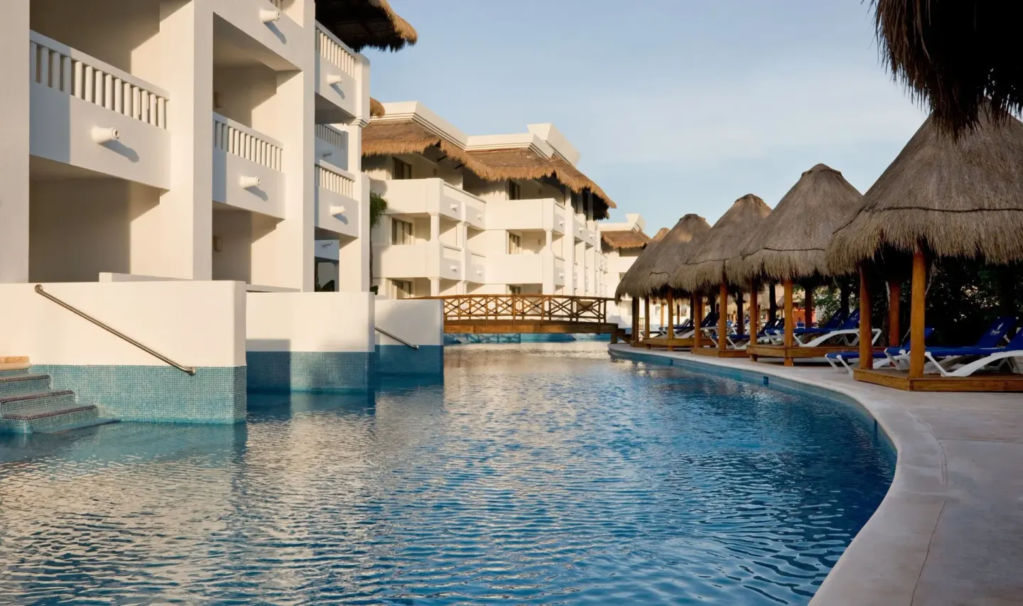 Curving pool beside guest room buildings and palapa shade at Grand Sunset Princess.