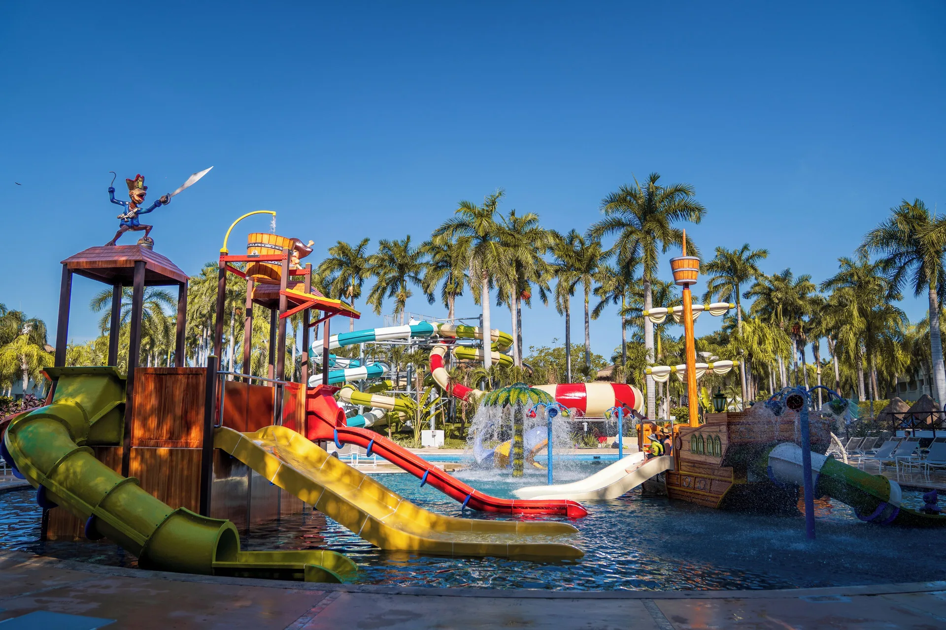 Water park play structures and slides at Grand Sunset Princess under palm trees.