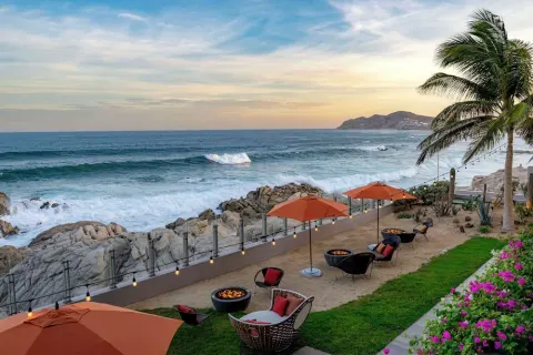 Coastal lawn with umbrellas, fire pits, and ocean waves at Grand Velas Los Cabos.