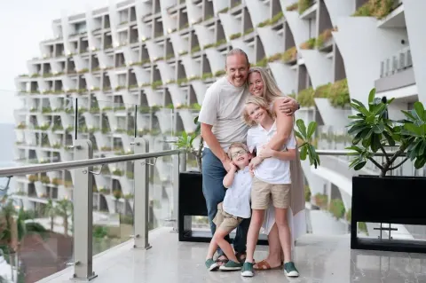 Family posing on a glass-railed balcony by guest room terraces at Grand Velas Los Cabos.