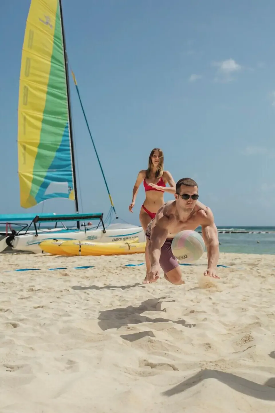 Guests play beach volleyball beside a catamaran at Grand Velas Riviera Maya.
