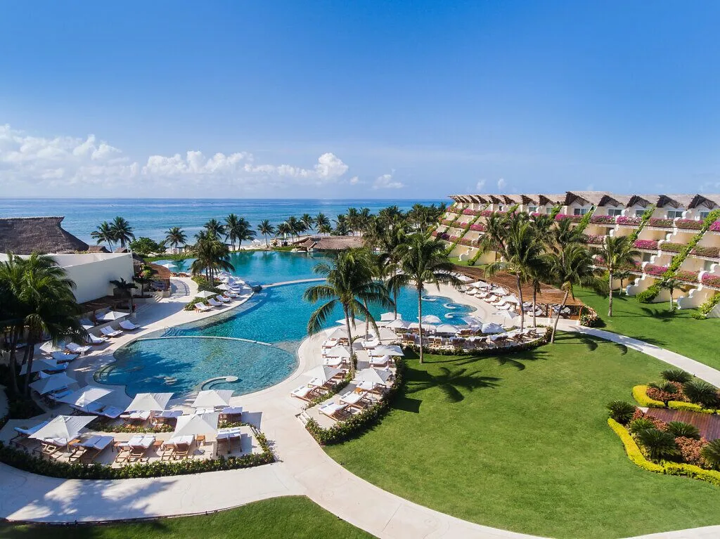 Wide daytime view of pools, lawns, palms and the ocean at Grand Velas Riviera Maya.