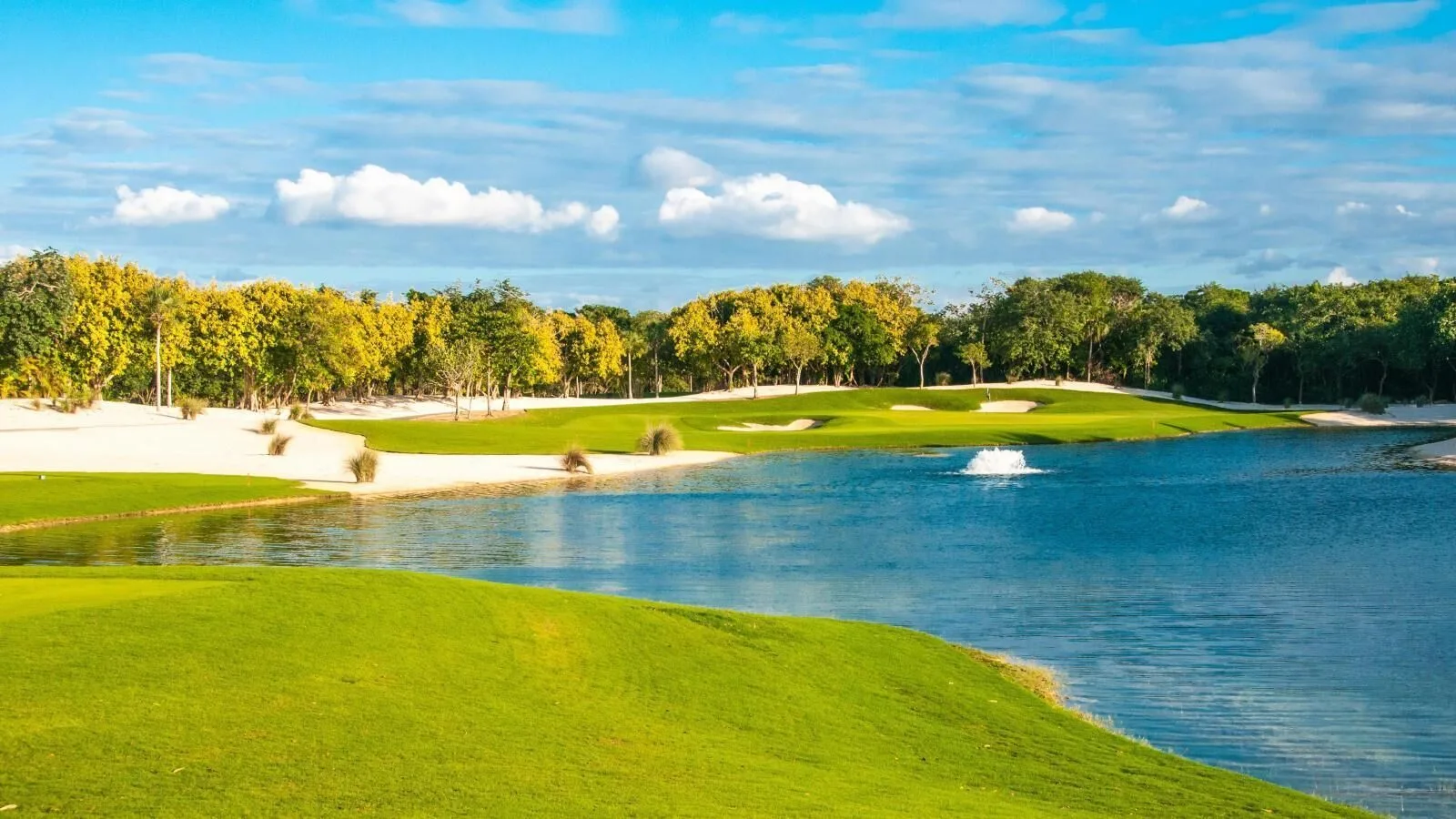 Golf course lake and fairway under a blue sky at Grand Velas Riviera Maya.