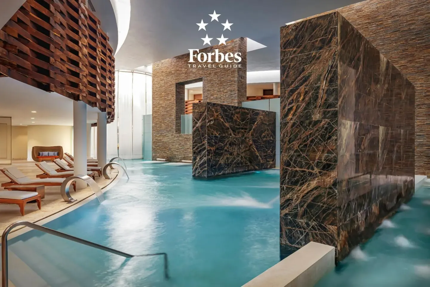 Indoor spa pool with loungers and stone water features at Grand Velas Riviera Maya.