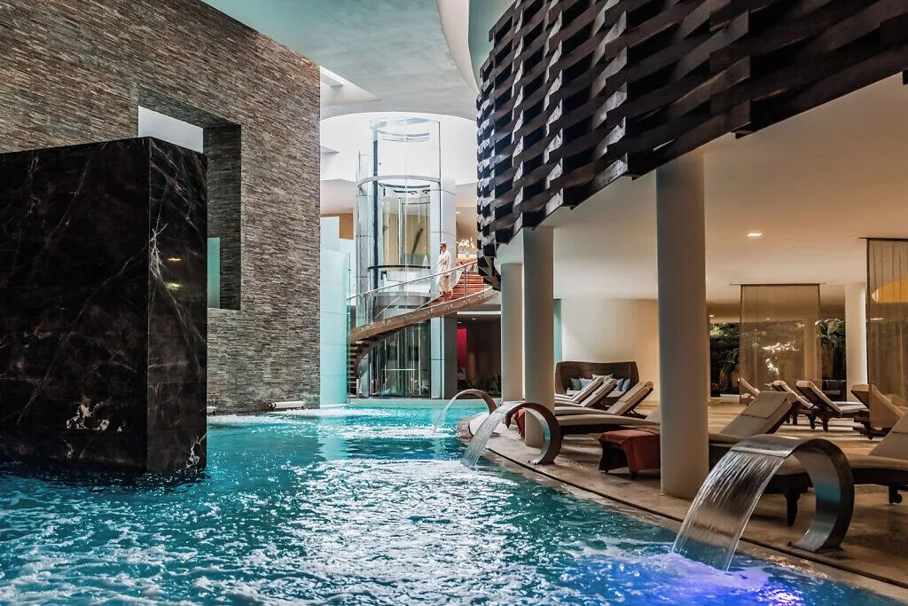 Indoor spa pool with water features and loungers at Grand Velas Riviera Maya.