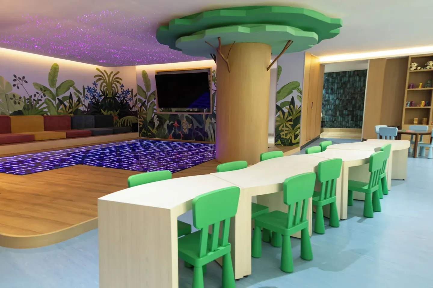 Kids' activity room at Grand Velas Riviera Maya with green chairs, tables, TV, and lighted play floor.