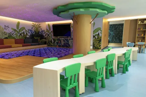 Kids' activity room at Grand Velas Riviera Maya with green chairs, tables, TV, and lighted play floor.