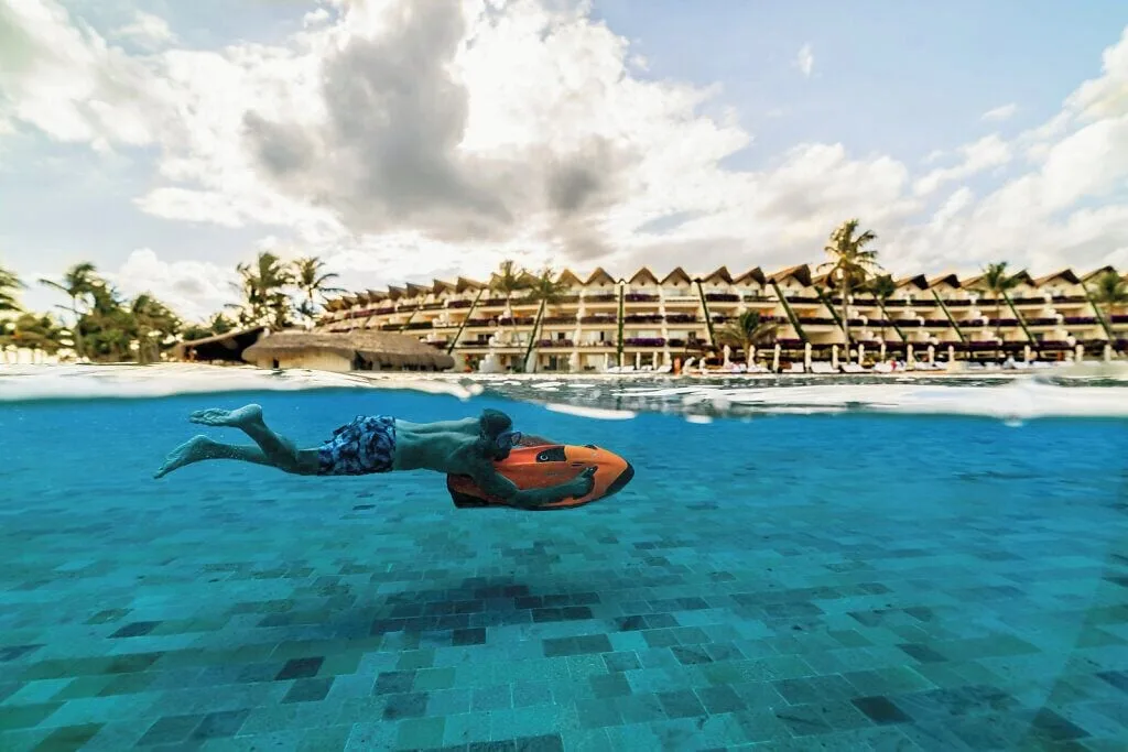 Guest rides an orange pool board underwater at Grand Velas Riviera Maya.