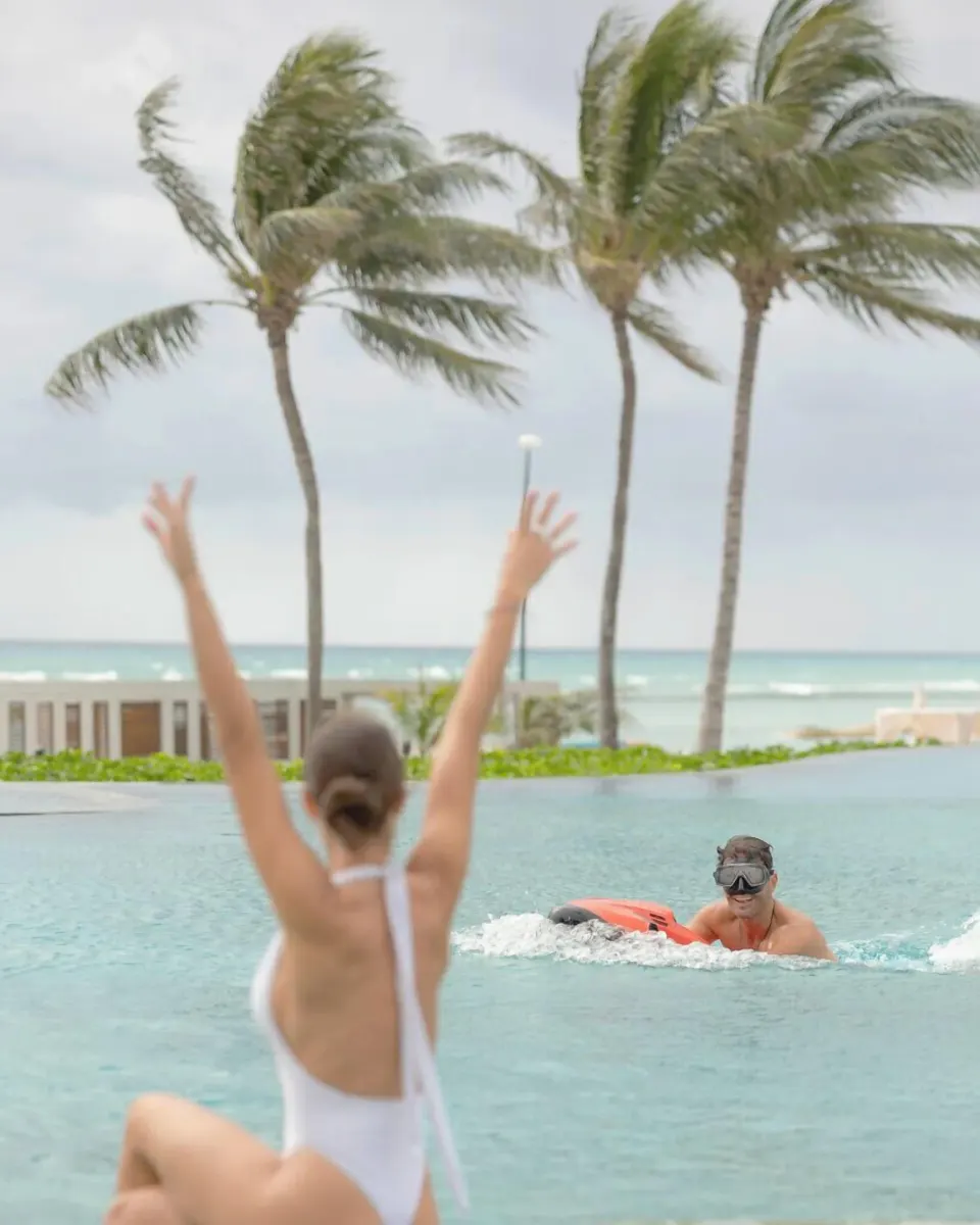 Guest with snorkel gear in the pool near palms and the sea at Grand Velas Riviera Maya.