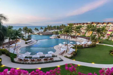 Twilight view of lit pathways, pools and oceanfront palms at Grand Velas Riviera Maya.