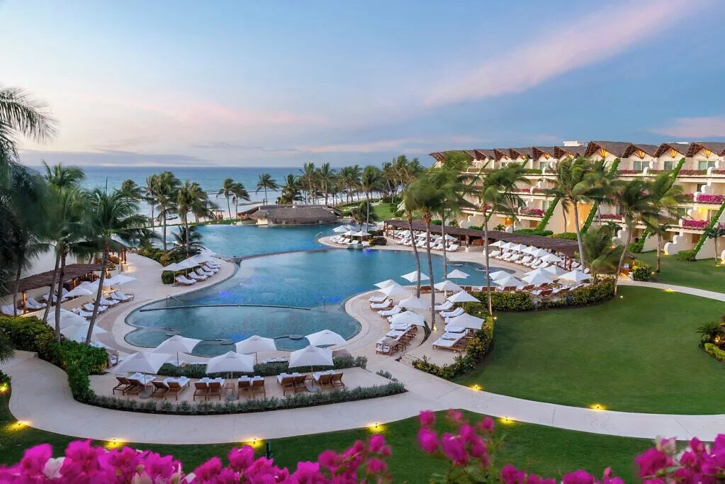 Twilight view of lit pathways, pools and oceanfront palms at Grand Velas Riviera Maya.