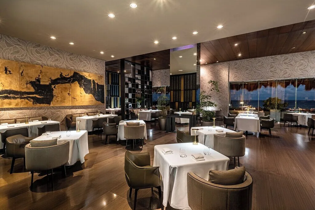 Elegant dining room with white-clothed tables and gold wall art at Grand Velas Riviera Maya.