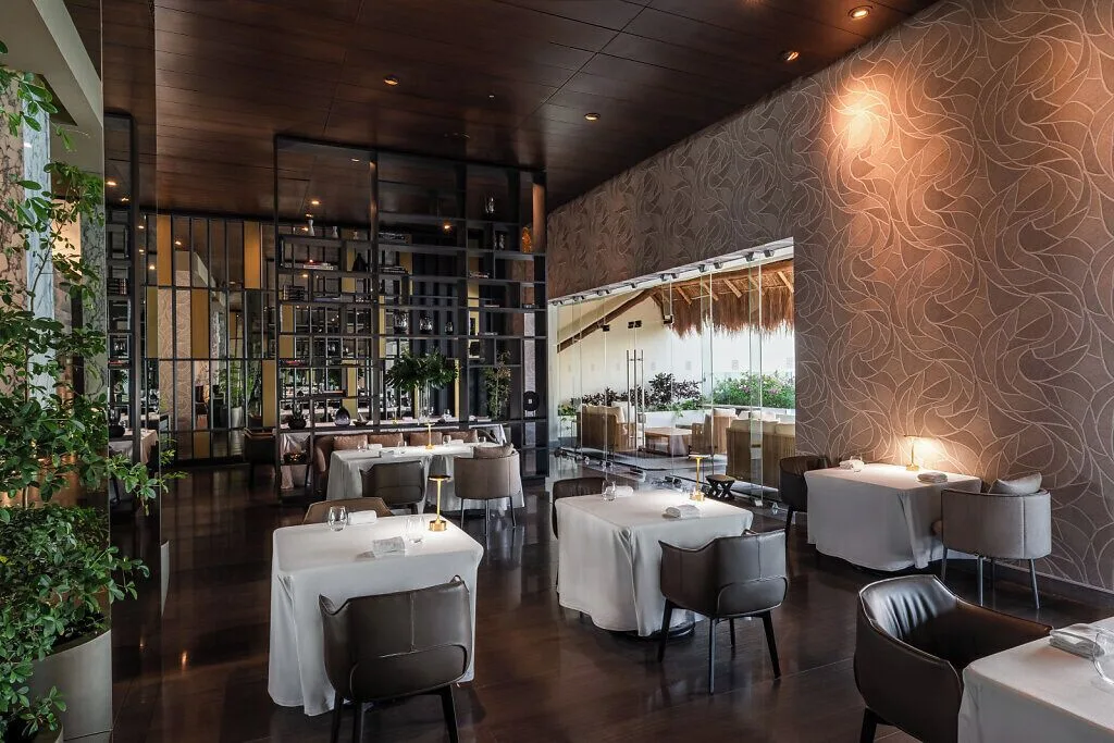 Modern dining room with white tablecloths and a glass wall at Grand Velas Riviera Maya.