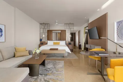 Grand Class Pool Suite with king bed, sofa, desk and warm yellow chairs at Grand Velas Riviera Maya.
