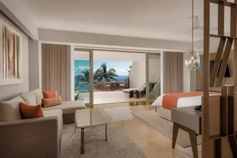 Grand Class Pool Suite with sofa, king bed and terrace facing palms and ocean at Grand Velas Riviera Maya.