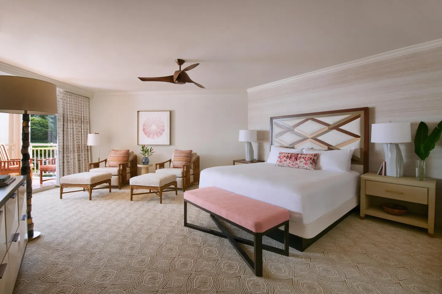 Guest room with a king bed, bench, lounge chairs, and balcony at Grand Wailea Maui.