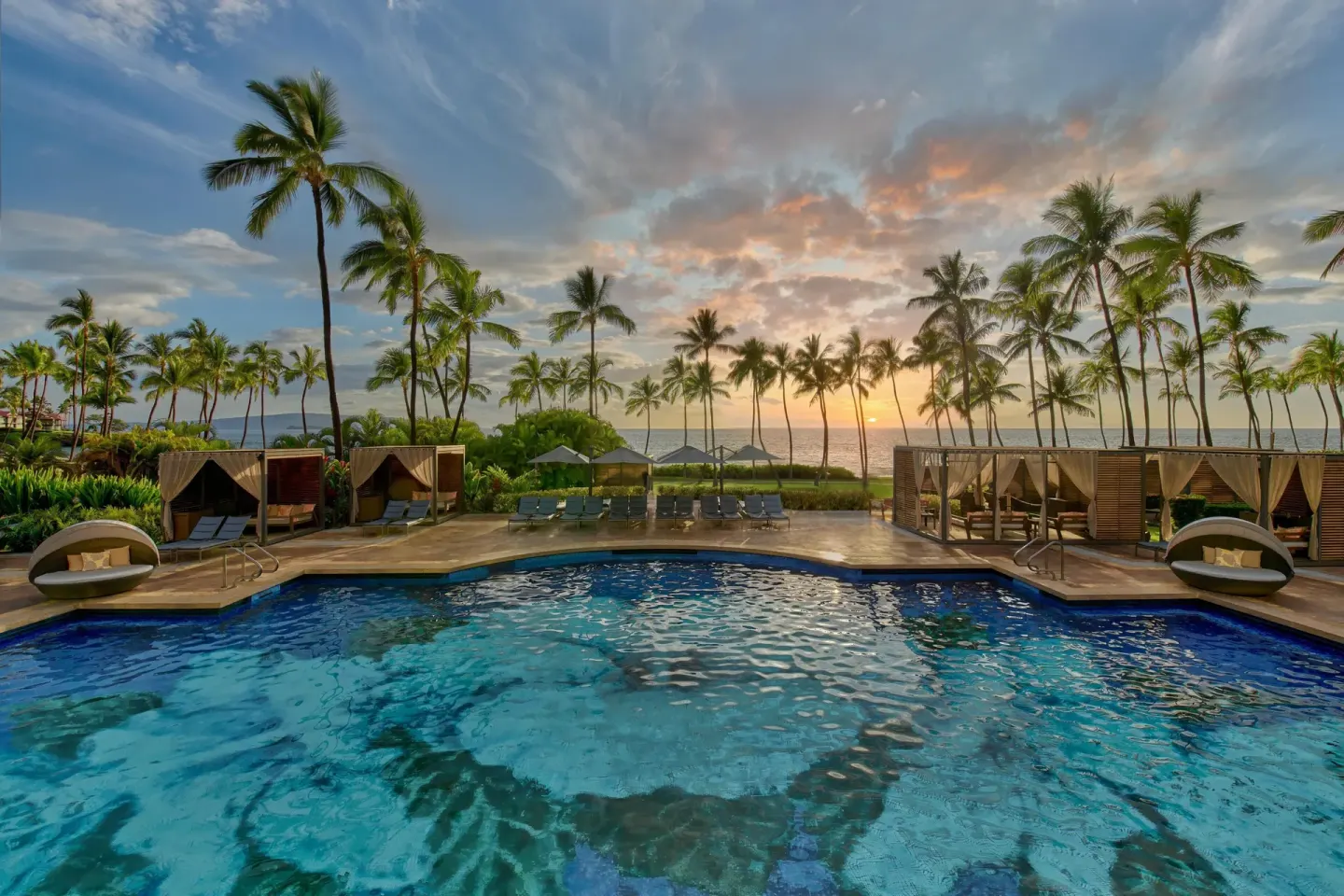 Oceanfront pool at sunset with cabanas and palm trees at Grand Wailea Maui.