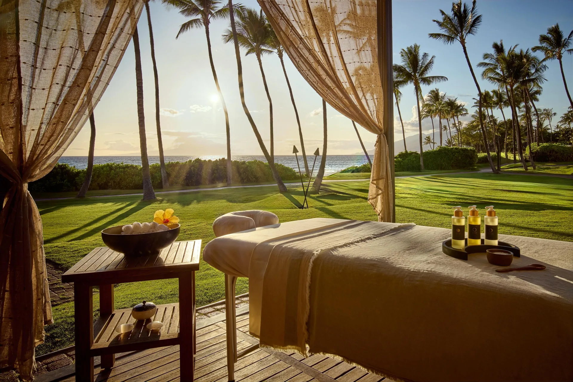 Outdoor spa massage setup with ocean, lawn and palm trees at sunset at Grand Wailea Maui.