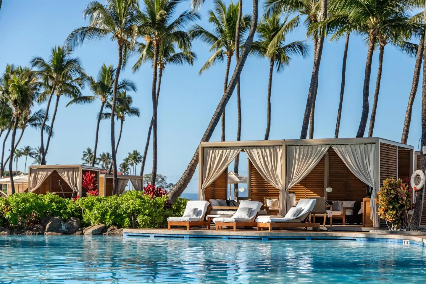 Poolside cabanas and lounge chairs beside the water at Grand Wailea Maui.
