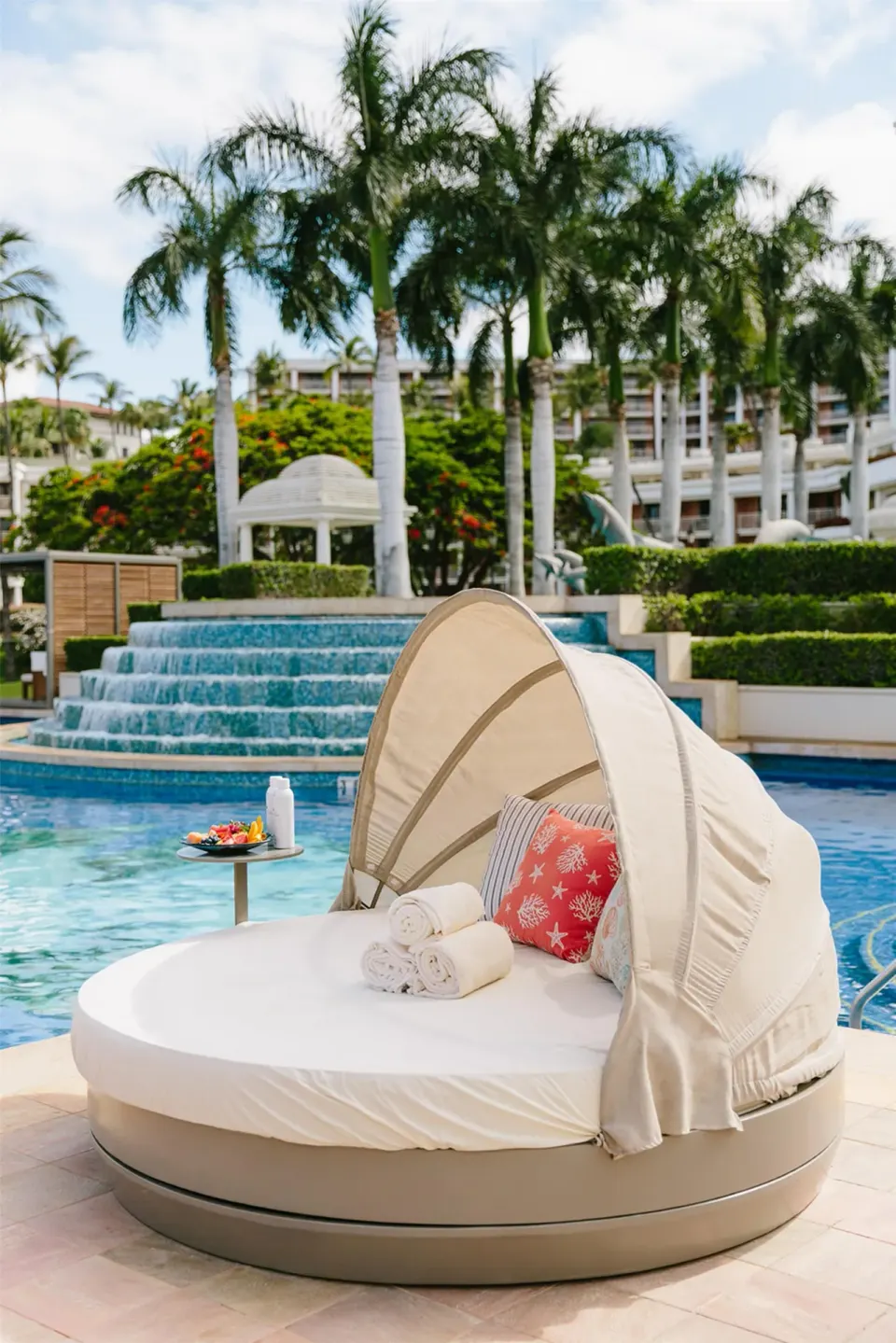 Round poolside daybed with canopy beside waterfall steps at Grand Wailea Maui.