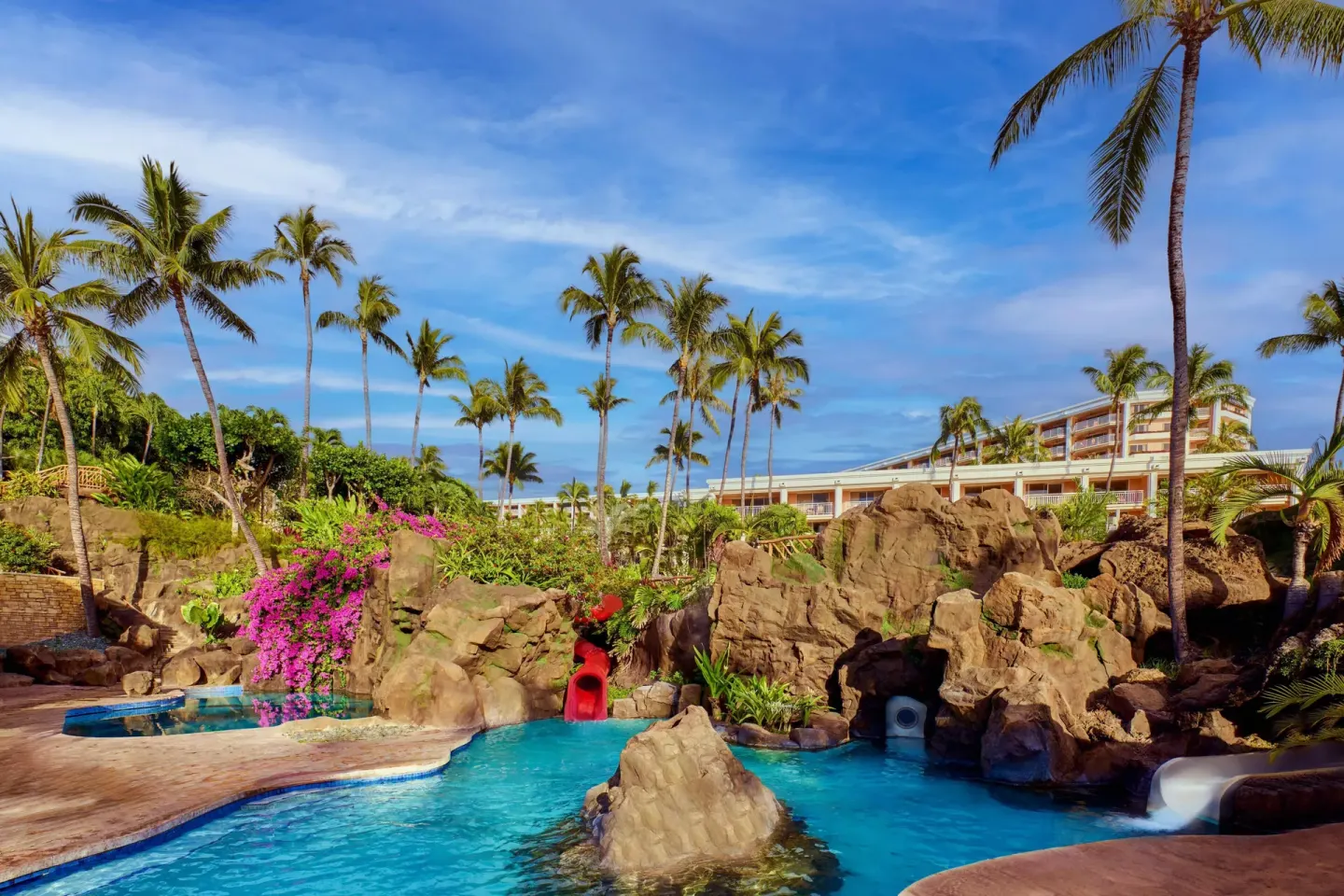 Resort pool with rock formations, waterslides, palms and guest buildings at Grand Wailea Maui.