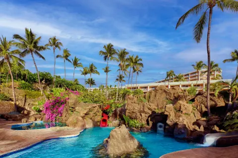 Resort pool with rock formations, waterslides, palms and guest buildings at Grand Wailea Maui.