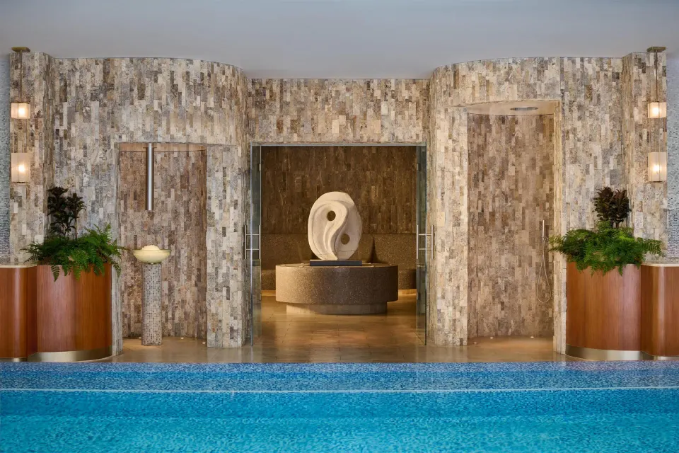 Spa pool with stone walls, showers, plants, and central sculpture at Grand Wailea Maui.