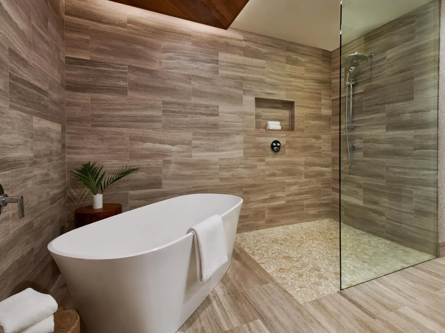 Stone-tiled bathroom with soaking tub and glass shower at Grand Wailea Maui.