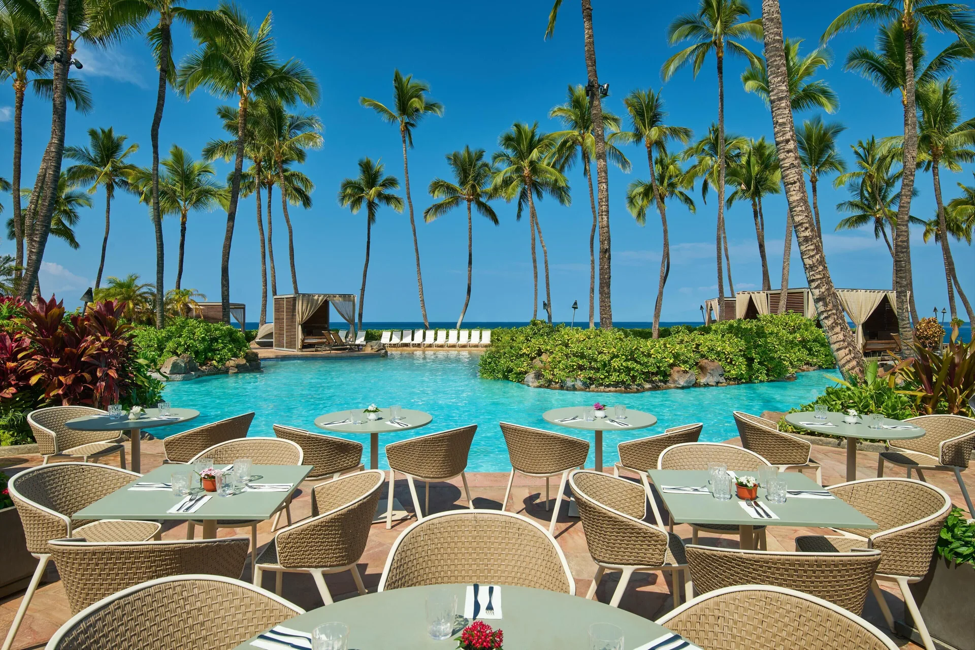Outdoor poolside dining tables beside palms and lagoon pool at Grand Wailea Maui.