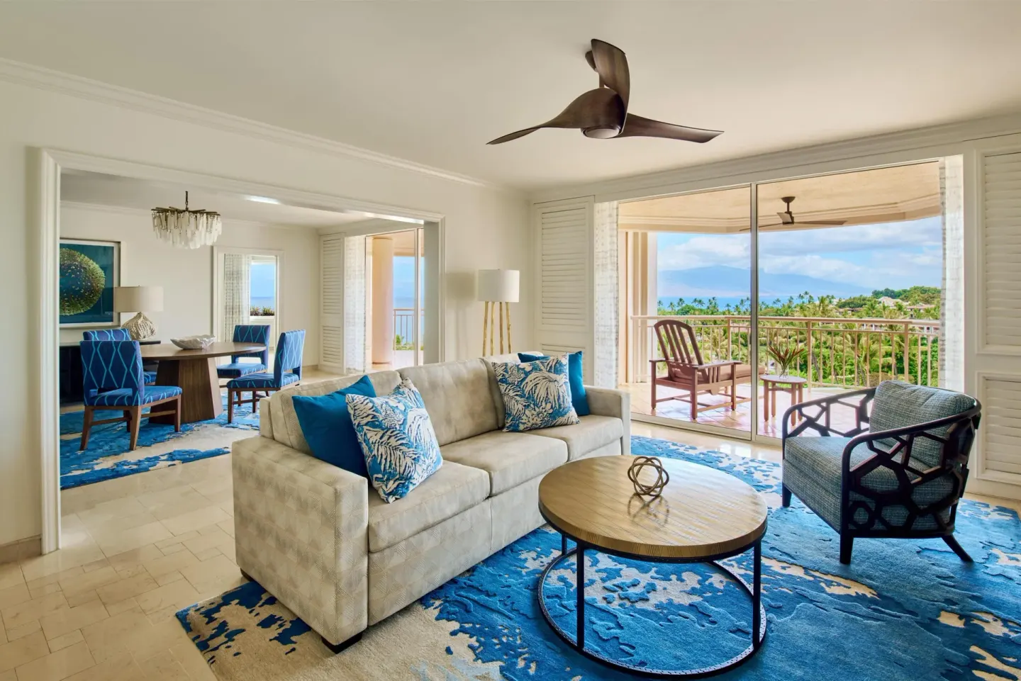 Living room in a Deluxe Suite at Grand Wailea Maui with sofa, dining area and balcony ocean view.