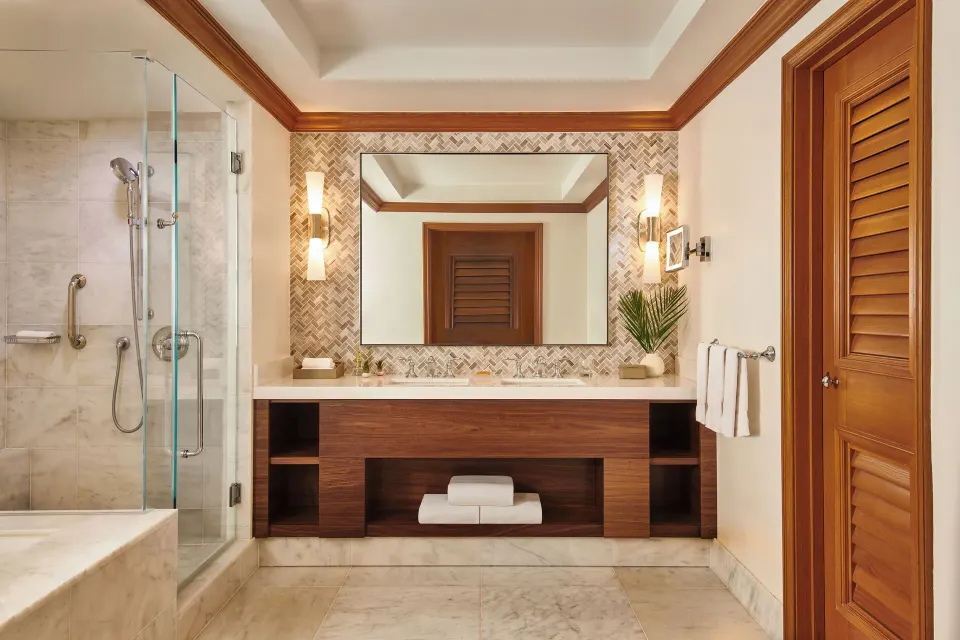 Royal Suite bathroom with glass shower, double vanity, and wood shutters at Grand Wailea Maui.