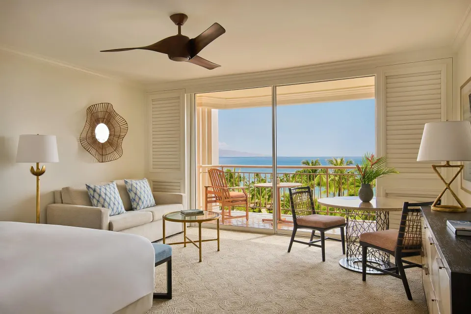 Ocean-view one-bedroom suite with bed, sofa, desk and balcony at Grand Wailea Maui.
