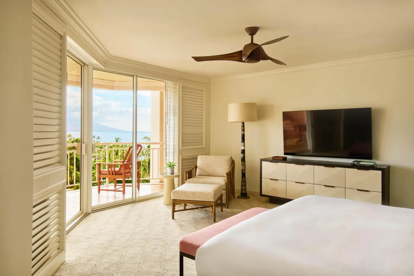 Bedroom with balcony, ocean glimpse, TV, lounge chair, and bed in an accessible suite at Grand Wailea Maui.