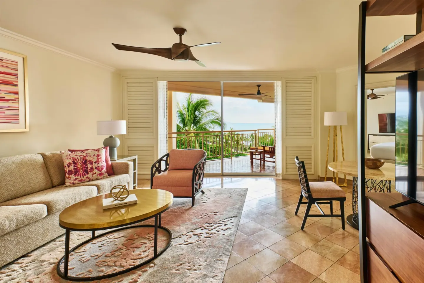 Living room with sofa, desk, TV, and balcony in an accessible garden view suite at Grand Wailea Maui.