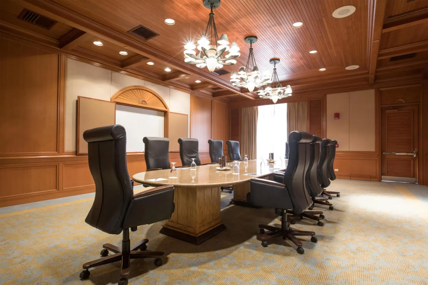 Boardroom with oval table, high-back chairs, chandeliers, and wood ceiling at Grand Wailea Maui.