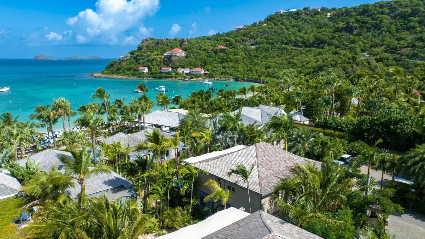 Aerial view of palms, resort rooftops, and turquoise bay at GYP SEA Saint Barth.