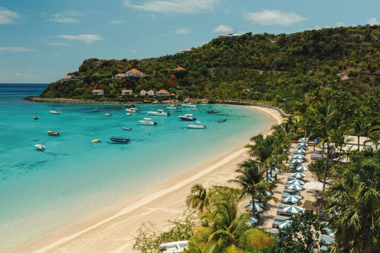 Curving sandy beach with boats and blue umbrellas near GYP SEA Saint Barth.