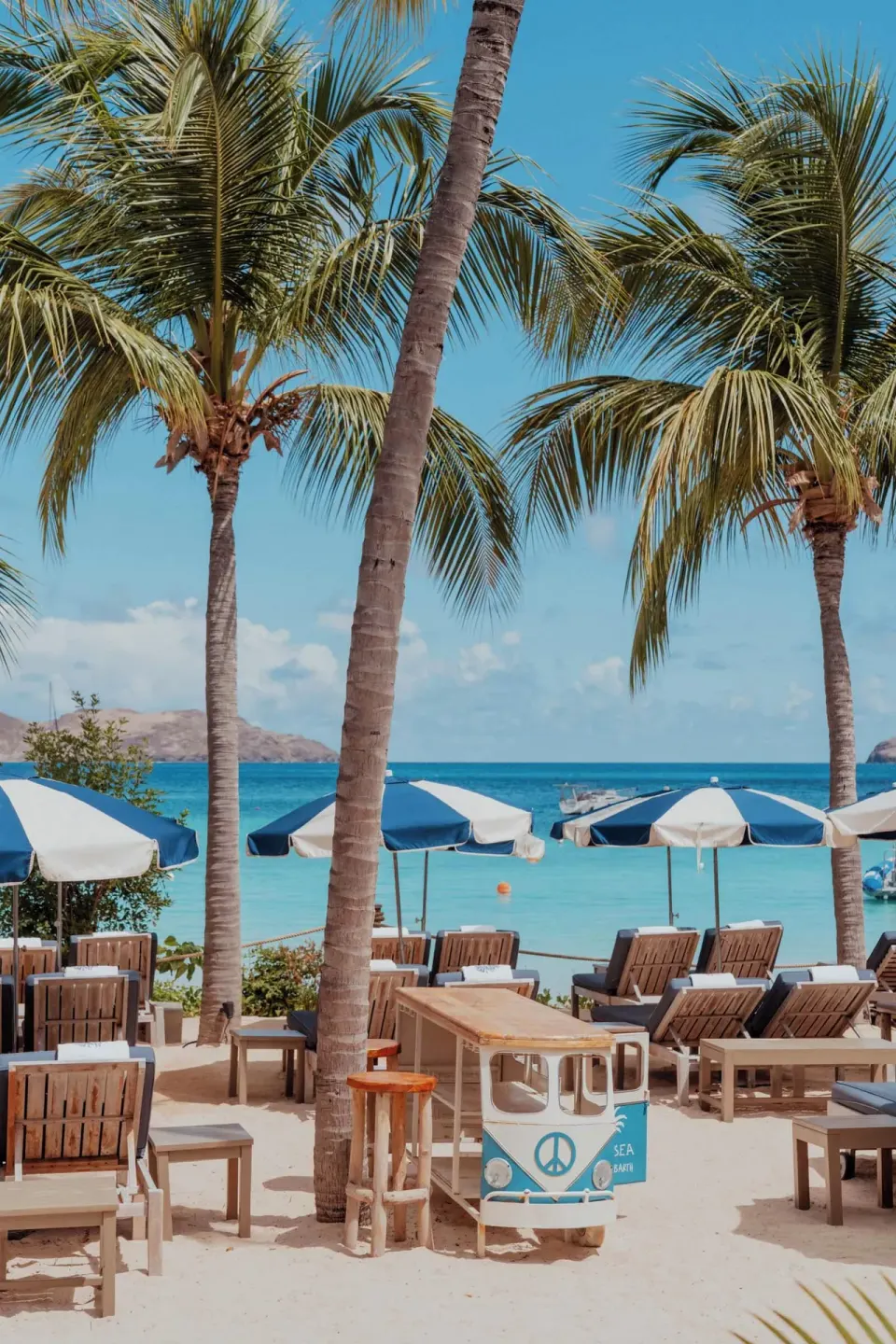 Beach loungers, palms, and blue umbrellas by the sea at GYP SEA Saint Barth.