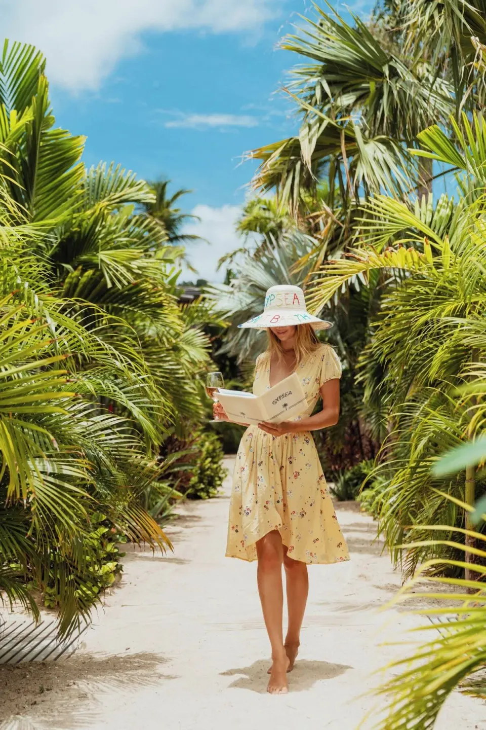 Palm-lined sandy path with a guest holding a drink at GYP SEA Saint Barth.