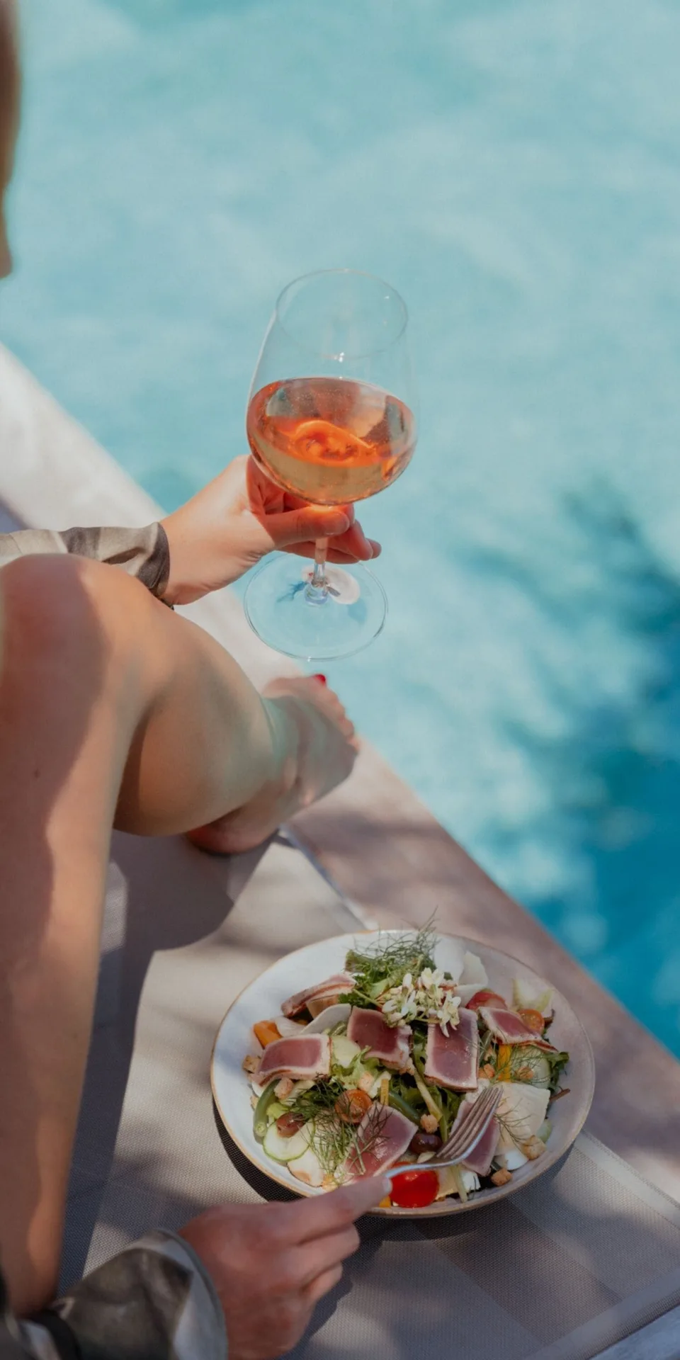Guest holding rosé beside a pool with a salad plate at GYP SEA Saint Barth.