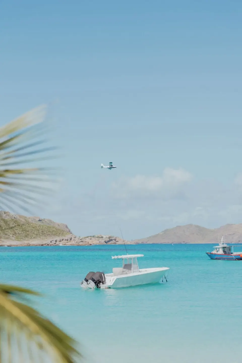 Boats floating on clear turquoise water with a seaplane overhead at GYP SEA Saint Barth.