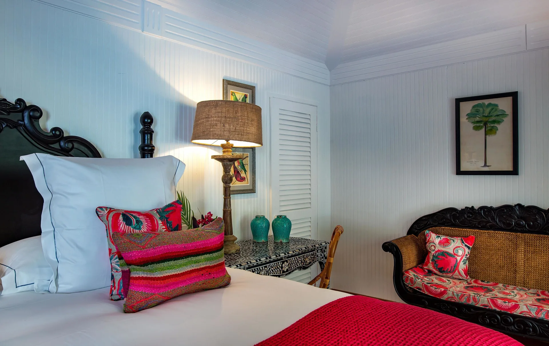 Bungalow king bed with red textiles and carved settee at GYP SEA Saint Barth.