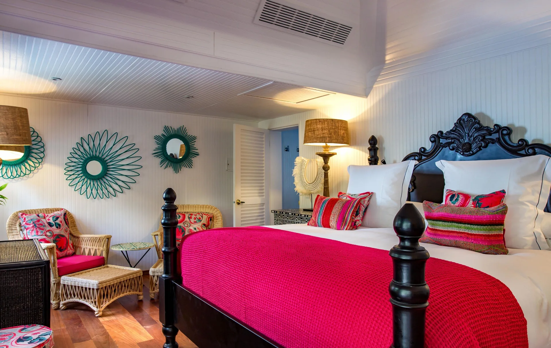 Bungalow king bed with red throw and carved headboard at GYP SEA Saint Barth.