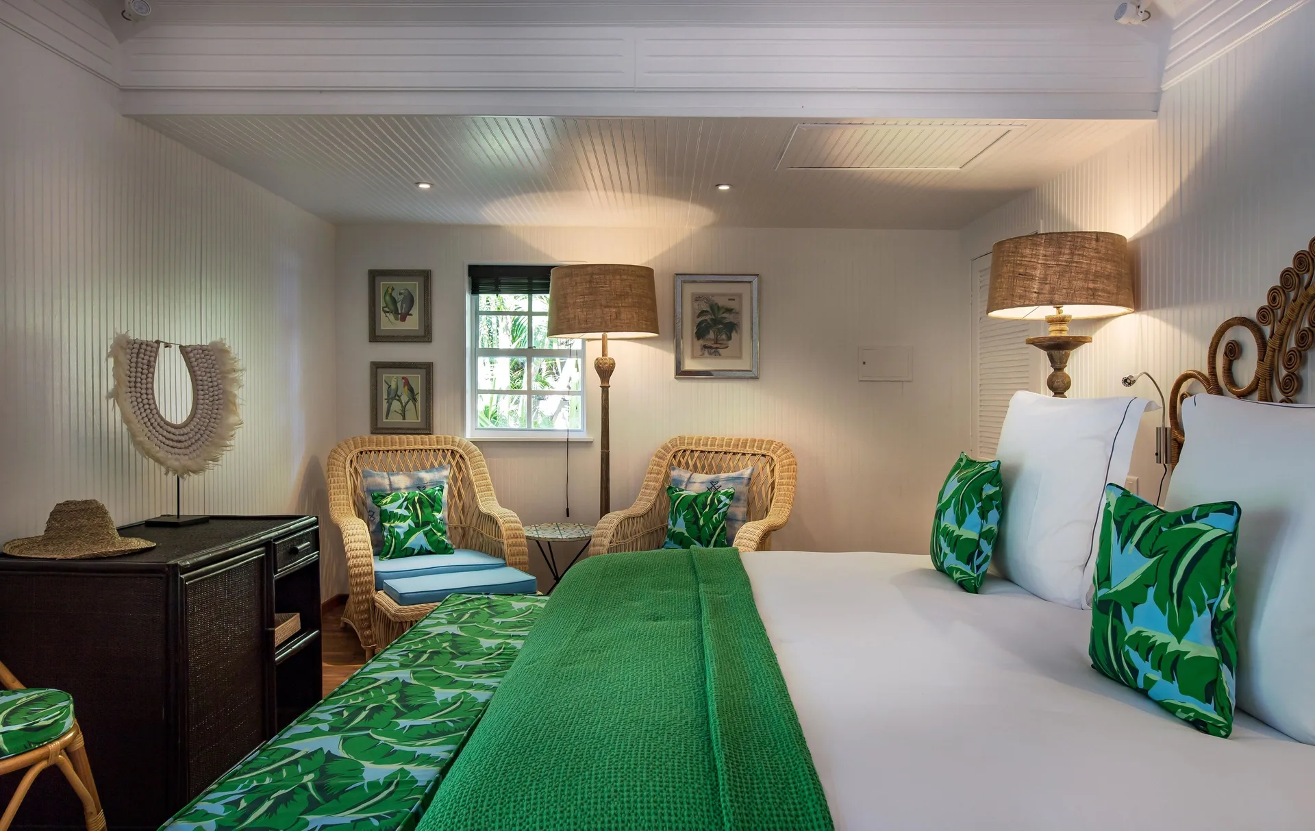 Bungalow king bed with wicker armchairs and green accents at GYP SEA Saint Barth.