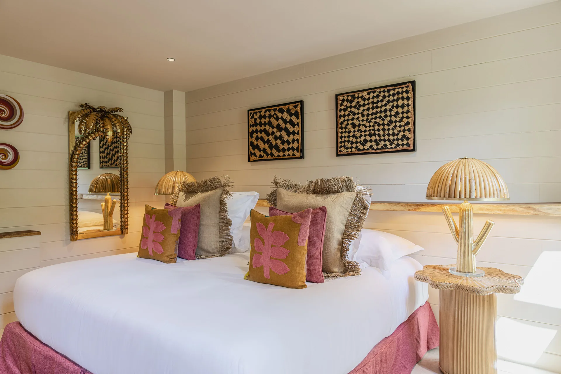 Bedroom with white bedding, pink bed skirt and woven lamps at GYP SEA Saint Barth.