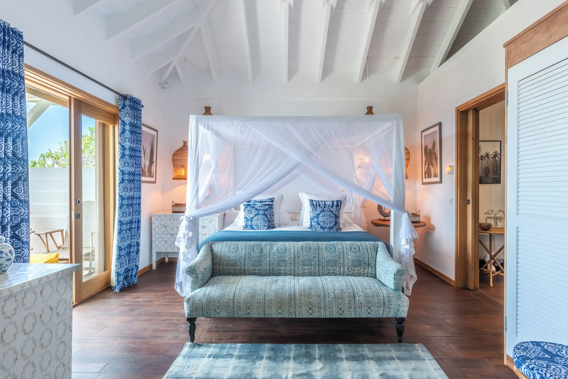 Havana Suite canopy bed with settee, balcony doors, and bathroom doorway at GYP SEA Saint Barth.