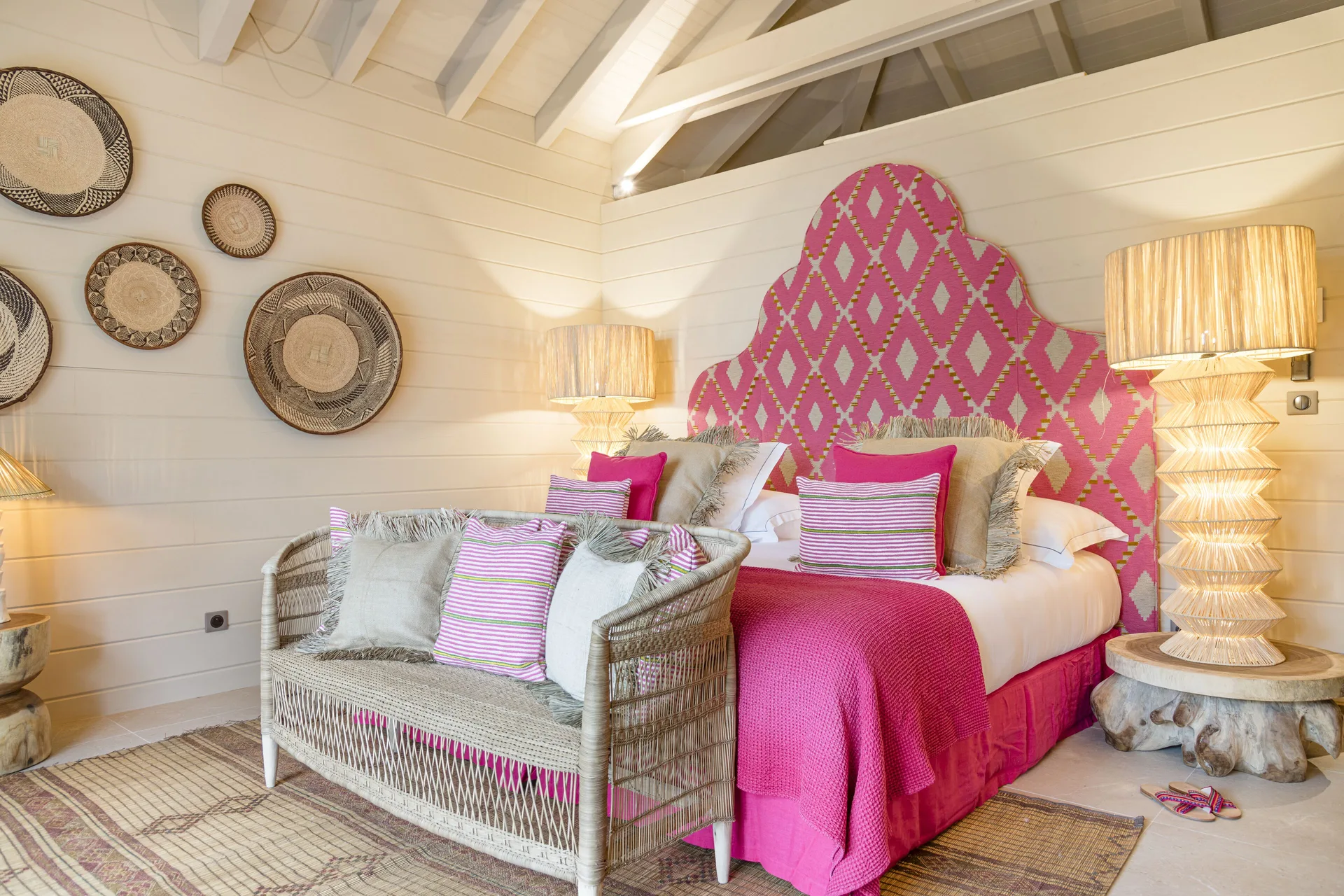 King bed with pink headboard and woven settee at GYP SEA Saint Barth.