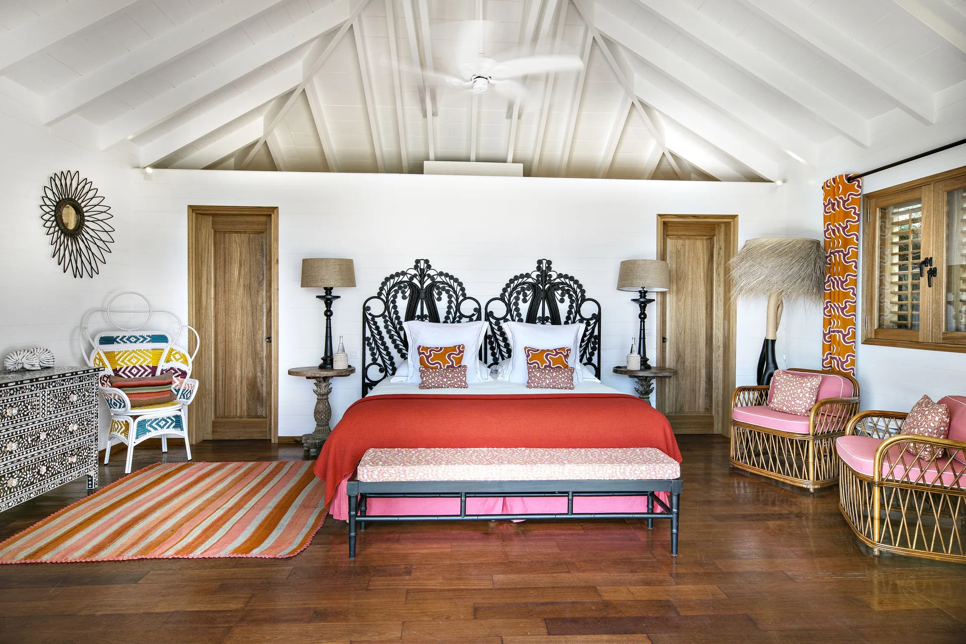 Villa bedroom with king bed, red coverlet, and wicker chairs at GYP SEA Saint Barth.